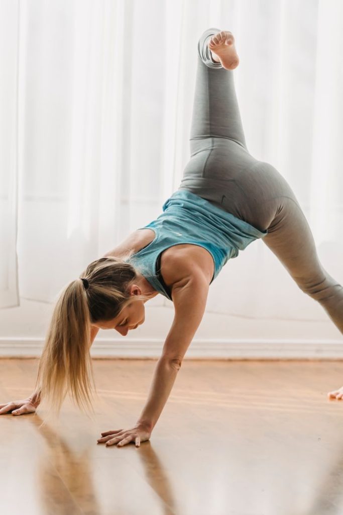 Determined young fit female with long blond hair in sportswear performing variation of Eka Pada Adho Mukha Svanasana while practicing yoga in studio
